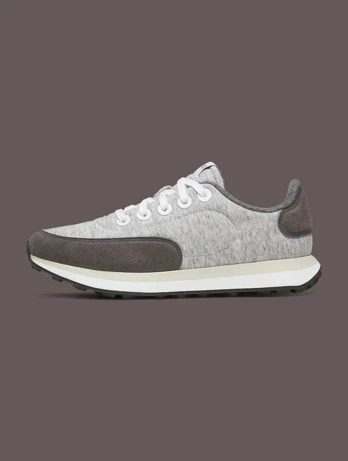 A grey Allbirds shoe shown in profile against a warm grey background.