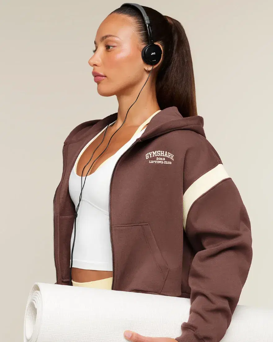 A person wearing a brown Gymshark jacket, with headphones and an exercise mat.